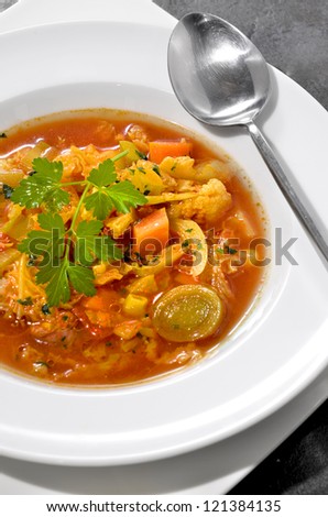 A rustic vegetable soup in a white porcelain bowl with stainless steel spoon