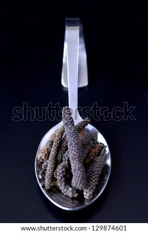 A teaspoon filled with Balinese long black peppercorns on a black background.