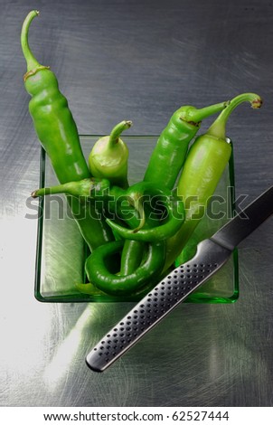 Fresh green chili peppers in a glass bowl on a brushed steel top with a japanese knife