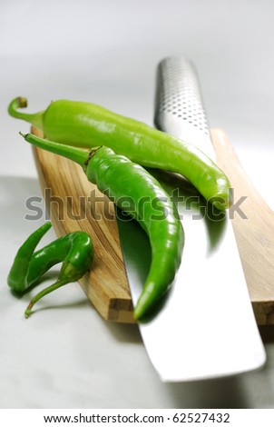 Fresh green chili peppers on a wooden board with a japanese knife