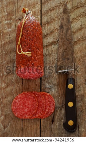 A salami sausage with an old carbon steel french knife and wooden board