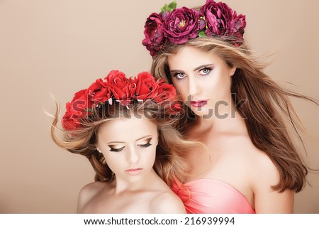 two young beautiful girl with expressive makeup and wreaths of flowers on her head on a beige background