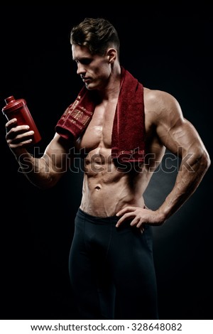Muscular fitness male bodybuilder holding protein shake bottle ready for drinking. Studio shot on dark background.