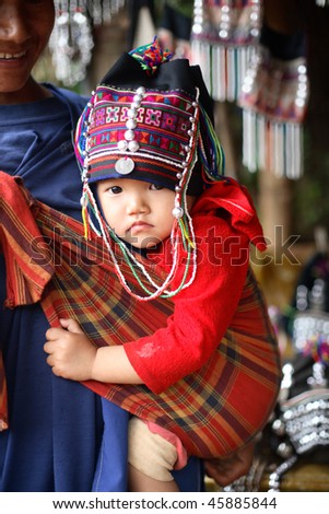 AKHA HILL TRIBE VILLAGE, THAILAND - AUG 24: Akha hill tribe woman carries a traditionally dressed child, Duo Soi, 1, August 24, 2007 in Akha hill tribe village, Thailand.
