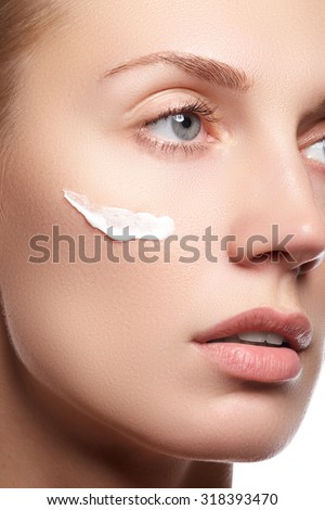 Beautiful young woman with clean fresh skin close-up. Beautiful woman face close up studio on white. Young woman with cosmetic cream on a clean fresh face. Skin care concept