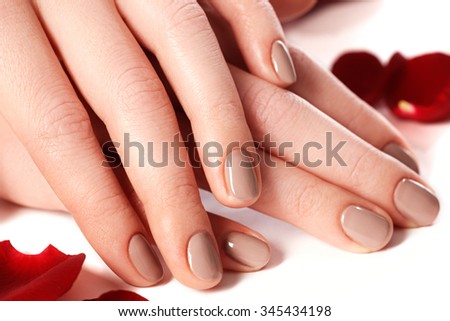 Beautiful female finger nails with natural nail closeup on petals. Perfect manicure. Woman hands with manicure natural nails closeup and rose. Skin and nail care.