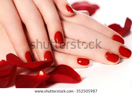 Beautiful female finger nails with red nail closeup on petals. Perfect manicure. Woman hands with manicure red nails closeup and rose. Skin and nail care