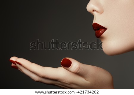 Beautiful young woman blowing a kiss from her hand. Model with perfect dark redl lips and manicured red nails
