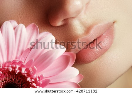 Lips with flower. Close-up beautiful female lips with bright lipgloss makeup. Perfect clean skin, light fresh lip make-up. Beautiful spa portrait with tender pink flower. Spa and cosmetics