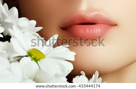 Lips with flower. Close-up beautiful female lips with bright lipgloss makeup. Perfect clean skin, light fresh lip make-up. Beautiful spa portrait with tender  flower. Spa and cosmetics