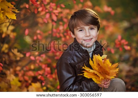 Happy 6 years old child boy and autumn leaves in a park. Kid has fun playing in fall leaves.