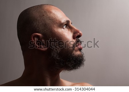 Serious bald man with beard in profile on dark studio background looking sides