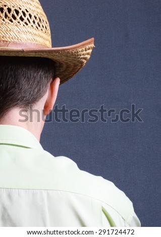 shoulder portrait of a man standing with his back to the camera with a straw hat on his head, on a gray background
