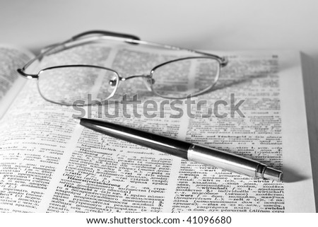 monochrome image of open dictionary with a pair of glasses and pen laying on top