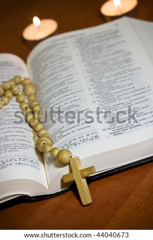 Old Cross and the Holy Bible laying on the table in front of a lighting candle
