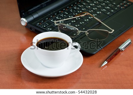 workplace with a laptop, mug of coffee, pen and glasses