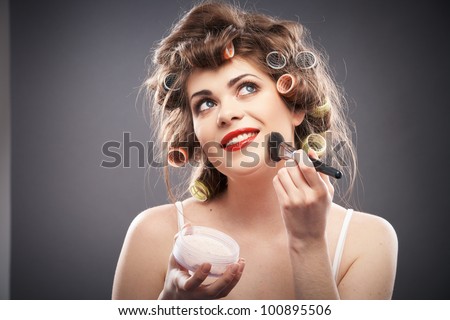 Close up portrait of a young woman with long hair on gray background making beauty face and hair style, applying powder at face. Smile happy girl  with make up accessories, studio isolated.