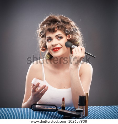 Portrait of a young woman with long curly hair on gray background isolated. Female Model Seating at table applying make up