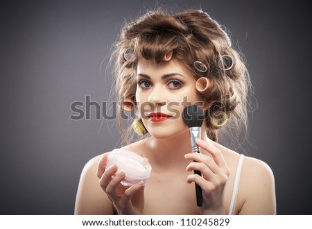Close up  portrait of a young woman with long hair on gray background making beauty face and hair style, applying powder at face. Smile happy girl  with make up accessories, studio isolated.