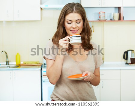 Portrait of young woman with coffee cup standing against kitchen interior background.