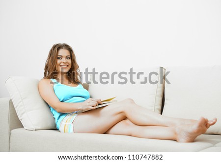 Young woman with long hair sitting  on couch at home with book.