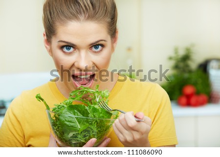 Happy Woman eating vegetarian food,  standing against  home kitchen interior background. Yellow color clothes. Woman Face close up portrait.