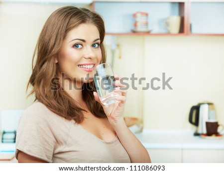 Portrait of happy  young woman drinking water against kitchen background.