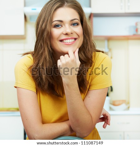 Portrait of young smiling woman sitting against kitchen background. Close up.