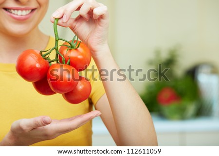 Woman hand holding tomato  at kitchen background. Yellow clothes.