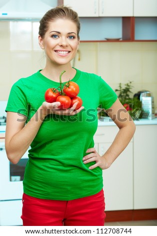 Young woman holding red tomato against home kitchen background.