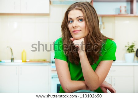 Portrait of smiling woman sitting in kitchen on a chair. Clothes of green color.
