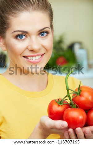 Young woman with tomato standing at kitchen. Close up healthy woman face.