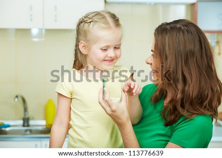Little girl drinking water in kitchen with young mother.