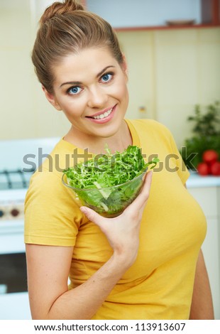 Woman with vegetarian food  standing against  home kitchen interior eating healthy food. Yellow color clothes.