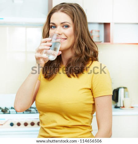 Woman with water glass standing against  home kitchen interior.