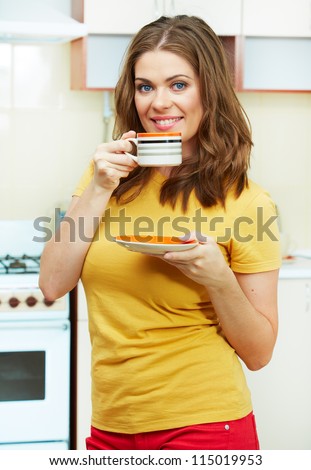 Portrait of young smiling woman holds a cup with coffee or tea against kitchen background. Yellow color clothes.