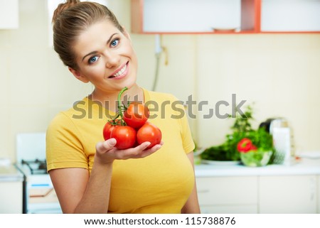 Young woman with tomato standing at kitchen.