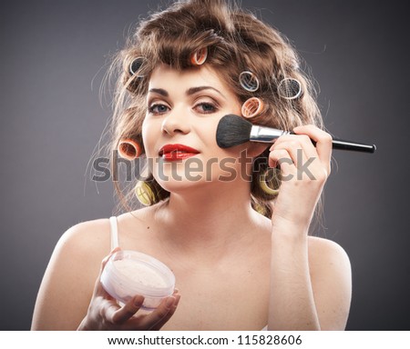 Close up portrait of a young woman with long hair on gray background making beauty face and hair style, applying powder at face. Smile happy girl  with make up accessories, studio isolated.