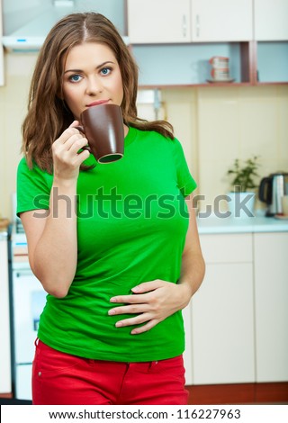 Portrait of young woman holds a cup with coffee or tea against kitchen background.