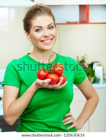 Young woman holding red tomato against home kitchen background.