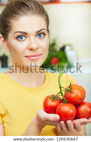 Young woman with tomato standing at kitchen. Close up healthy woman face.