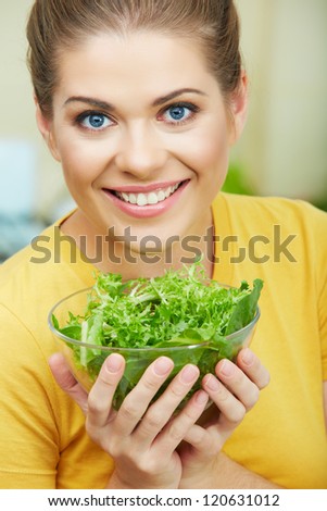 Woman with vegetarian food  standing against  home kitchen interior eating healthy food. Yellow color clothes. Close up woman face portrait.