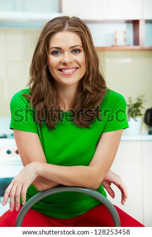 Portrait of smiling woman sitting in kitchen on a chair. Clothes of green color.