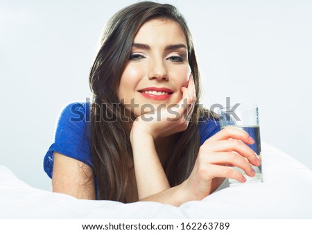 Young smiling woman lying in bed, hold water glass. Female model.