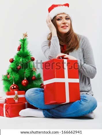 Santa woman seat near Christmas tree with christmas gift. Isolated smiling woman in santa hat.
