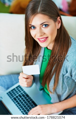 Young woman sitting on couch with laptop, credit card. Home portrait.
