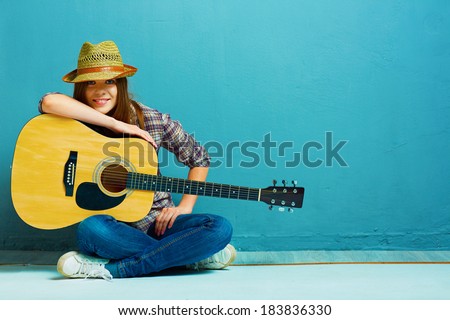 Teenager girl guitar play sitting on a floor. Blue background. Country style.