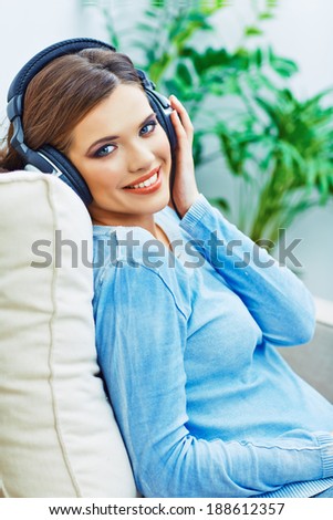 Portrait of young smiling woman sitting on sofa, listening music. Relaxed girl.