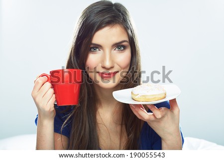 Woman eating donut in bed with coffee cup. Smiling girl.