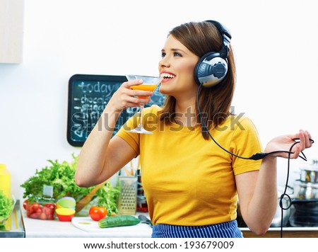 Woman cooking with fun. Smiling Girl drinking juice in kitchen and listen music.